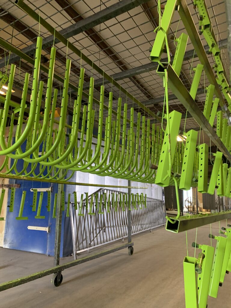 Bright green powder-coated metal components hanging in the FX Industries shop