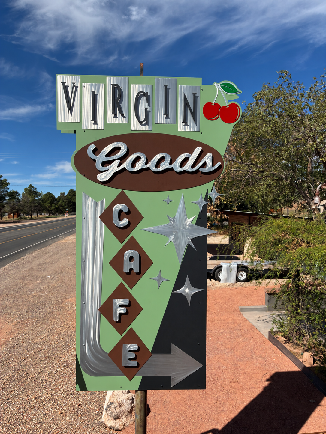 Virgin Goods Cafe roadside sign with raised lettering, cherry artwork, stars, and an arrow